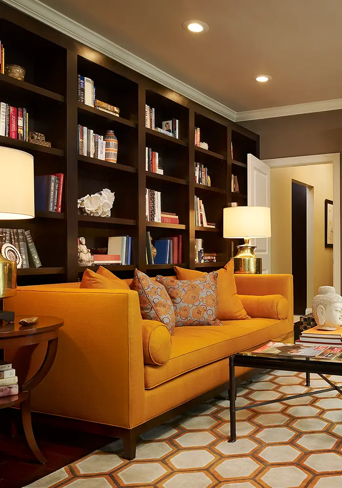 A dramatic & bold living room space with a wall-sized book & display shelf, a modern bright sofa and geometric rug