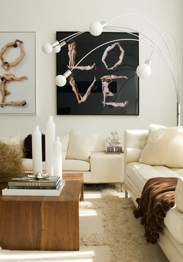 A bright and modern living room space with an arched lamp, a mix of natural elements, and large modern art on the walls showing the word "LOVE" spelled out in human forms